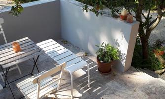 A cozy garden area with a table and chairs. In the background, plants and a terrace can be seen.