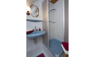 A small bathroom with a shower and a sink. The walls are tiled, and there are towels in red.