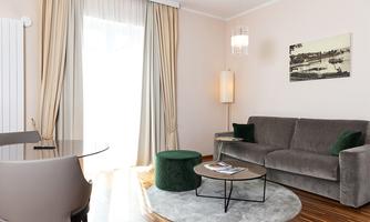 A modern living room with a gray sofa, a round table, and stylish decorative elements. Plenty of daylight pours in through the large windows, creating an inviting atmosphere.