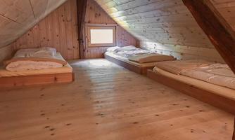 A cozy attic with wooden paneling. There are three single beds and a window that provides natural light.