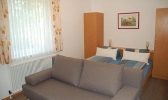 A simple room with a sofa and two single beds. Bright curtains and a picture on the wall create a pleasant atmosphere.