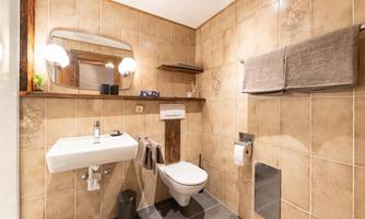 A modern bathroom with bright tiles and a sink. There is a toilet, towels, and mirror lighting.