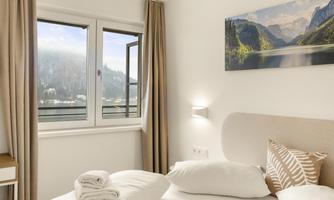 A bright bedroom with a cozy bed and decorative pillows. A picturesque mountain landscape can be seen through the window.