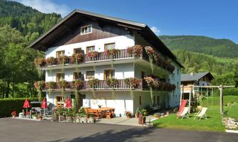 A cozy house with flower boxes and sun umbrellas. In the background, picturesque mountains and a green landscape can be seen.