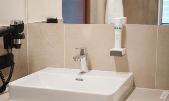A modern bathroom with a white sink on a wooden base. In the background, towels and a hairdryer are visible.