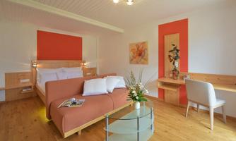 A modern room with a cozy bed and an orange wall. The room is bright and friendly, with a glass table and subtle decorations.