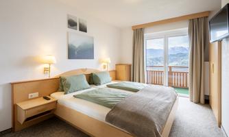 A bright and cozy bedroom with two single beds. The room features a balcony with a beautiful view of the mountains.