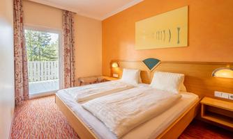 A cozy bedroom with a double bed and warm color tones. The room has access to a balcony and is decorated with soft furniture.