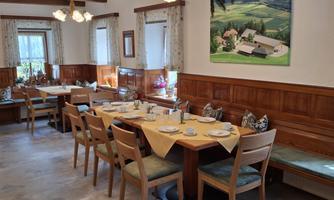 A cozy dining room with wooden furniture and laid tables. A picture of a rural landscape hangs on the wall.