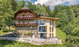 A modern house in alpine style with a beautiful garden. The facade has flower balconies and is surrounded by green trees.