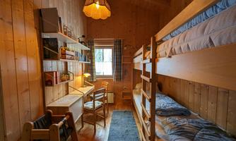 A cozy room with wooden walls and bunk beds. A desk and a lamp create an inviting atmosphere.
