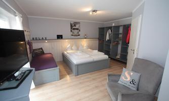A modern bedroom with a double bed and a cozy armchair. There is a relaxed atmosphere with bright colors and a wardrobe for clothes.