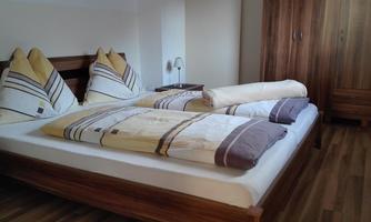 A cozy bedroom with a double bed and modern pillows. The room has a warm wooden floor and a simple decor.