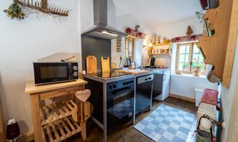 A cozy kitchen with modern appliances and wooden shelves. Bright windows provide enough light and an inviting atmosphere.
