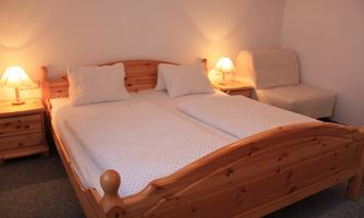 A cozy bedroom with a wooden double bed. Next to the bed are nightstands with lamps and a comfortable armchair.