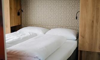 A cozy bedroom with a double bed and modern wooden furniture. The walls are in a simple design with a subtle pattern.