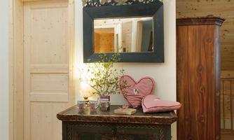 A rustic table with a decorative flower vase stands against a wall. Above it hangs a beautiful mirror, and next to it stands a wooden cabinet.
