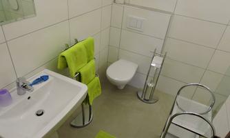 A modern bathroom with white tiles and green towels. It features a sink, a toilet, and a cozy look.