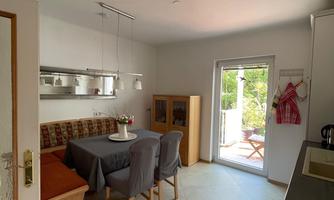 A bright and modern kitchen with a dining area and a large window. The room is designed to be friendly and inviting.