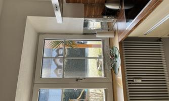 A bright kitchen with a window overlooking a garden. On the countertop, there is a bowl of fruit and a kettle.
