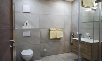 A modern bathroom with tiles in neutral colors. There is a shower, a sink, and a toilet, as well as fresh towels.
