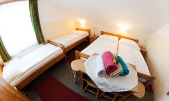 A cozy room with two single beds and one double bed. Freshly folded towels are lying on the table.