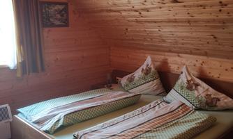 A cozy bedroom with two single beds and wood paneling. The room has windows with curtains and a calm atmosphere.