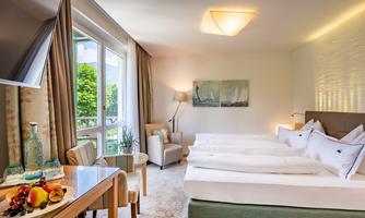 A bright and modern hotel room with a large window and comfortable beds. Fresh fruit and water are on the table.