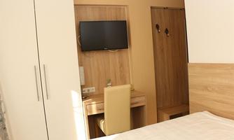 A modern bedroom with a TV on the wall and a desk. The furniture is in warm wood tones.