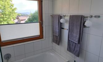 A modern bathroom with a bathtub and gray towels. Through the window, there is a beautiful view of the landscape.