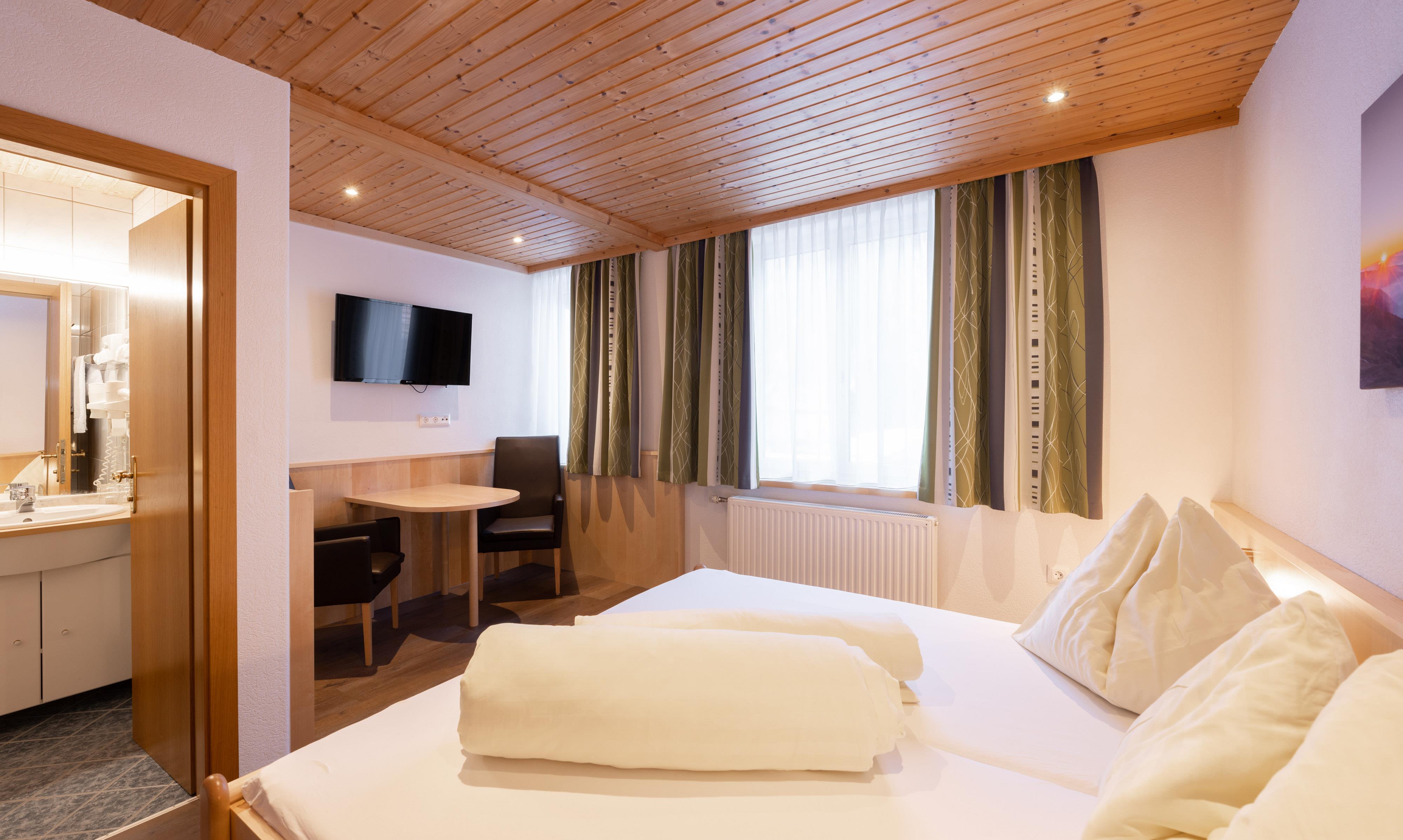 A cozy hotel room with a double bed and bright colors. There is a small dining area and a bathroom that is accessible through a door.