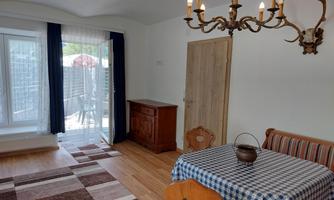 A bright room with a dining table and a wooden sideboard. Large windows let in a lot of light, and there is access to the terrace.