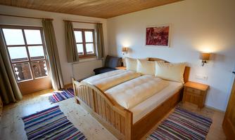 A cozy bedroom with a wooden double bed and colorful carpets.  
Windows with curtains let in plenty of light and create a friendly atmosphere.