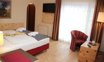 A cozy hotel room with a double bed, an armchair, and a table. Large windows let in plenty of daylight.