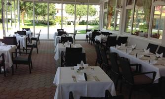 An elegant restaurant with white tablecloths and chairs. The room is bright and offers a beautiful view of the outdoor area.