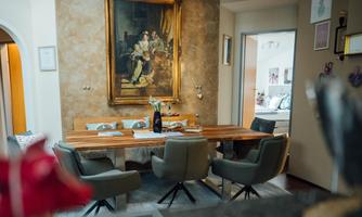 An elegant dining area with a wooden table and comfortable chairs. A large painting hangs on the wall, decorating the space.