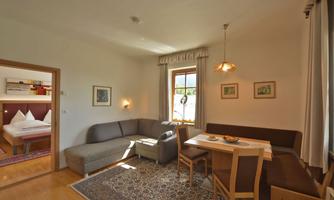 A cozy living area with a dining table and a couch. In the background, a bedroom with aesthetic decor can be seen.