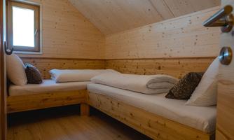 A cozy wooden room with two beds and a warm, inviting atmosphere. The window lets in natural light and creates a bright ambiance.