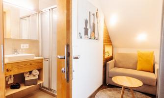 A modern room with a cozy sofa and a small table. On the left, there is a bathroom area with a sink and a shower.
