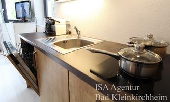A modern kitchen with a sink, cooking utensils, and a dishwasher. In the background, there is a television.