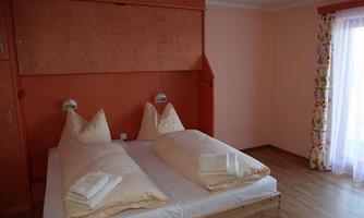 A cozy bedroom with a double bed and bright bedding. The walls are in a soft orange, and a window lets in plenty of natural light.