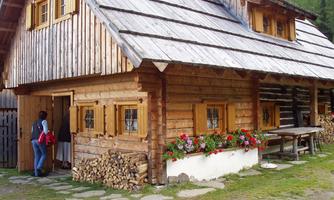 A cozy wooden house with a steep roof and colorful windows. In front of the house, flowers are growing, and wooden logs are stacked.