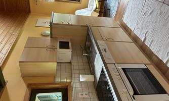 A bright kitchen with wooden shelves and modern appliances. The room has an inviting atmosphere and large windows for natural light.