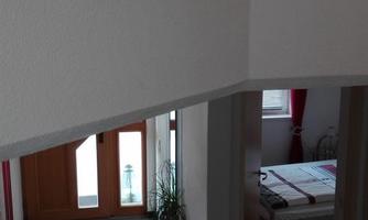 A modern hallway with a red carpet runner and large windows. There is a view of a sunny living area in the background.