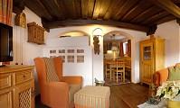 A cozy living room with wooden ceilings and warm colors. There are comfortable armchairs and a dining area in the background.