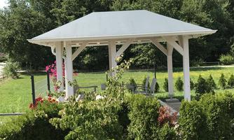 A beautiful pavilion surrounded by green shrubs and trees. The sky is clear and blue.