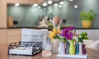 A stylish kitchen table with colorful flower vases and fresh flowers. Modern kitchen elements are visible in the background.