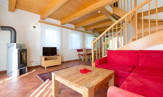 A cozy living room with a red sofa and wooden table. Large windows provide plenty of daylight and an inviting atmosphere.