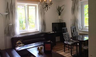 A modern living room with a brown sofa and an elegant table. There is a television and a dining table with striped chairs.
