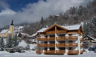 A picturesque winter landscape with a wooden hotel and snow-covered mountains. In the background, there is a church and tall fir trees.
